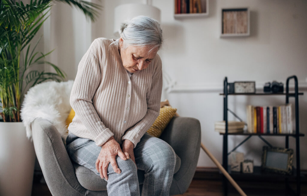 Elderly woman with osteoarthritis struggles to move from a lounge chair.