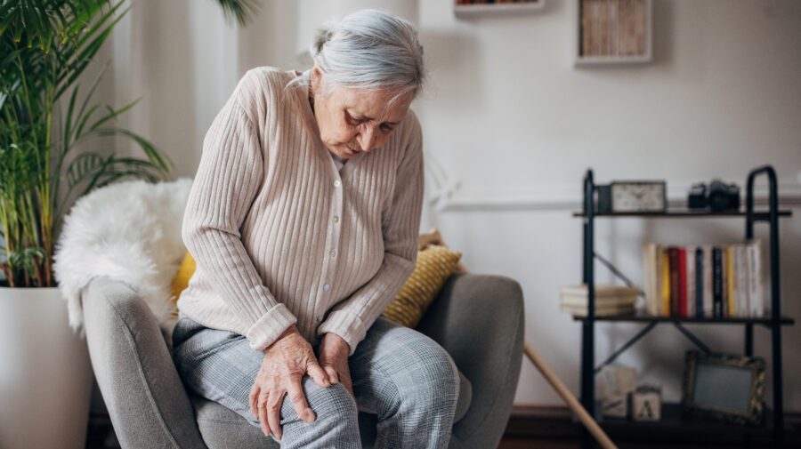 Elderly woman with osteoarthritis struggles to move from a lounge chair.