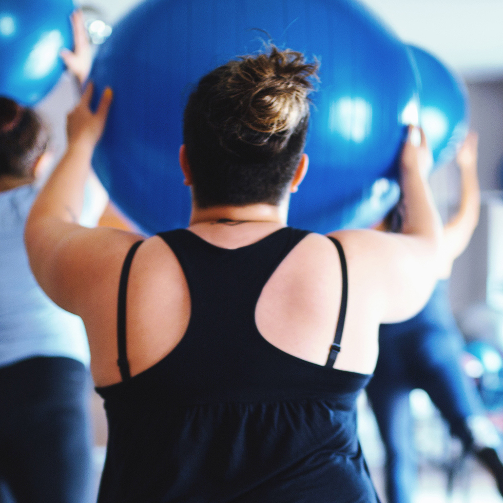Rear view of overweight women working out together with a fitness ball and step platforms in the gym.
