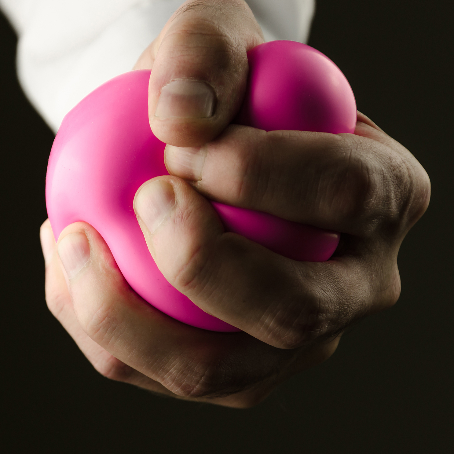 Arm or hand with a white shirt pressure pink anti stress ball in the dark or black background
