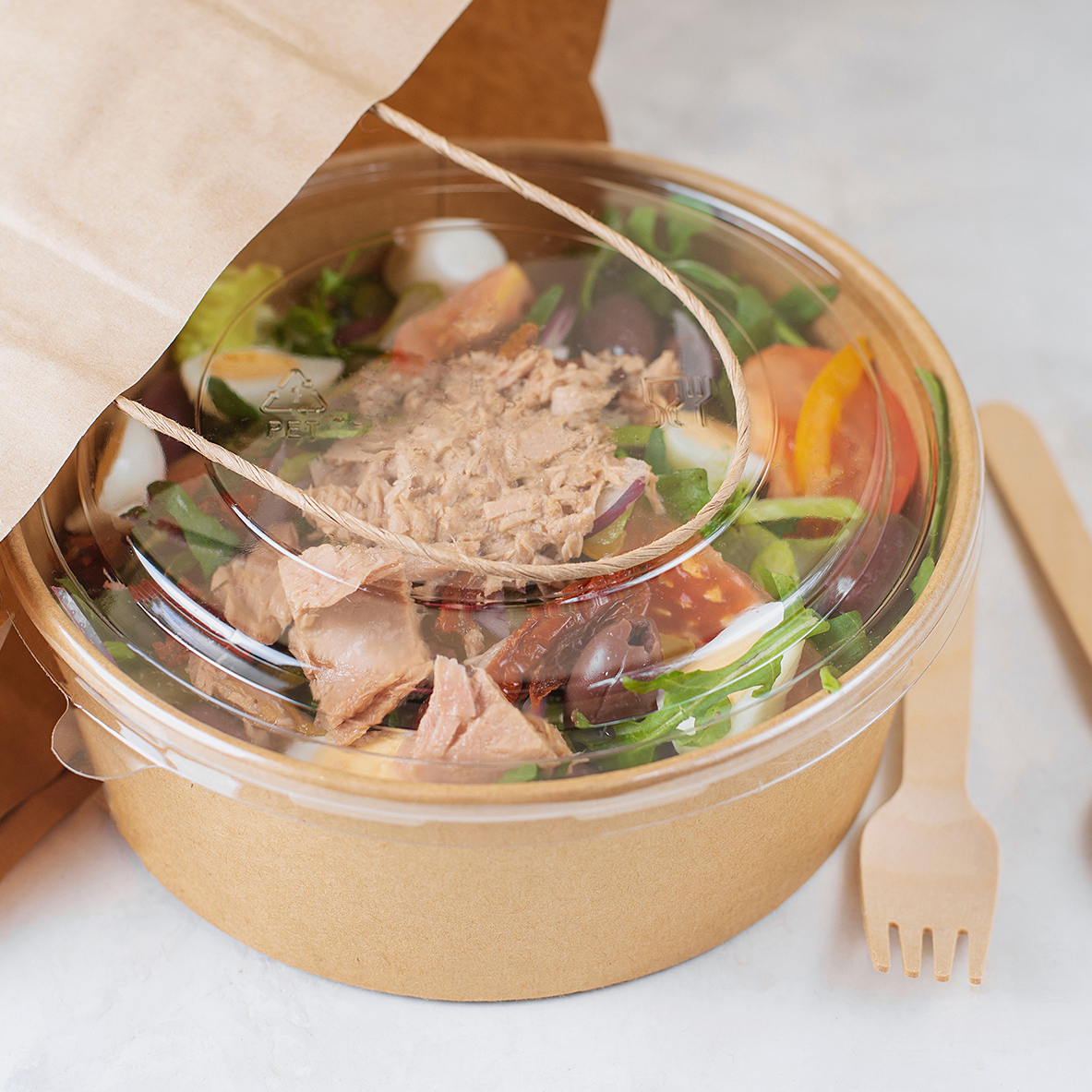 Fish diet salad with tuna, tomatoes, arugula on light background. Healthy vegetarian lunch. Concept eco restaurant delivery, environment protection. Take away food in brown paper craft plate.